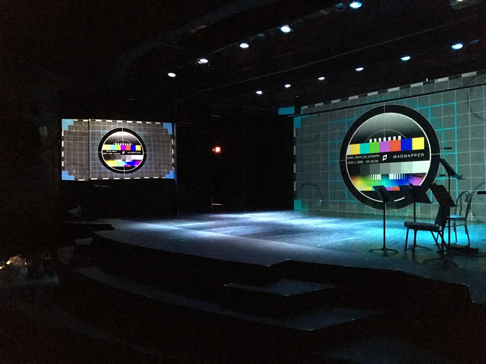 An empty stage during focus, with MadMapper alignment grids and colour bars projected onto two separate surfaces — a flat upstage screen and a curved wall